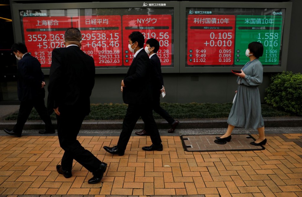 Passersby wearing protective face masks walk past an electronic board displaying world stock indexes, amid the coronavirus disease (COVID-19) pandemic...