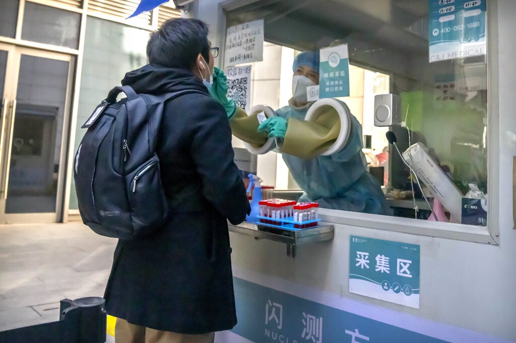 A worker administers a COVID-19 test while standing inside a mobile coronavirus testing facility at an office complex in Beijing, Wednesday, Dec. 1, 2...