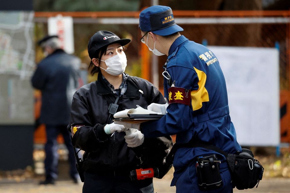 A police investigator speaks to another person at the site where a stabbing incident happened at an entrance gate of Tokyo University in Tokyo, Japan ...