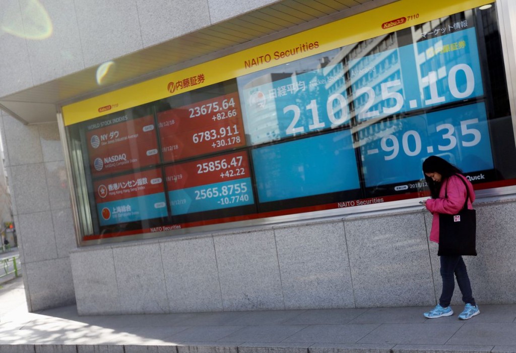 A woman stands in front of a screen displaying Japan's Nikkei share average, U.S. and other countries' stock market indicators outside a broke...
