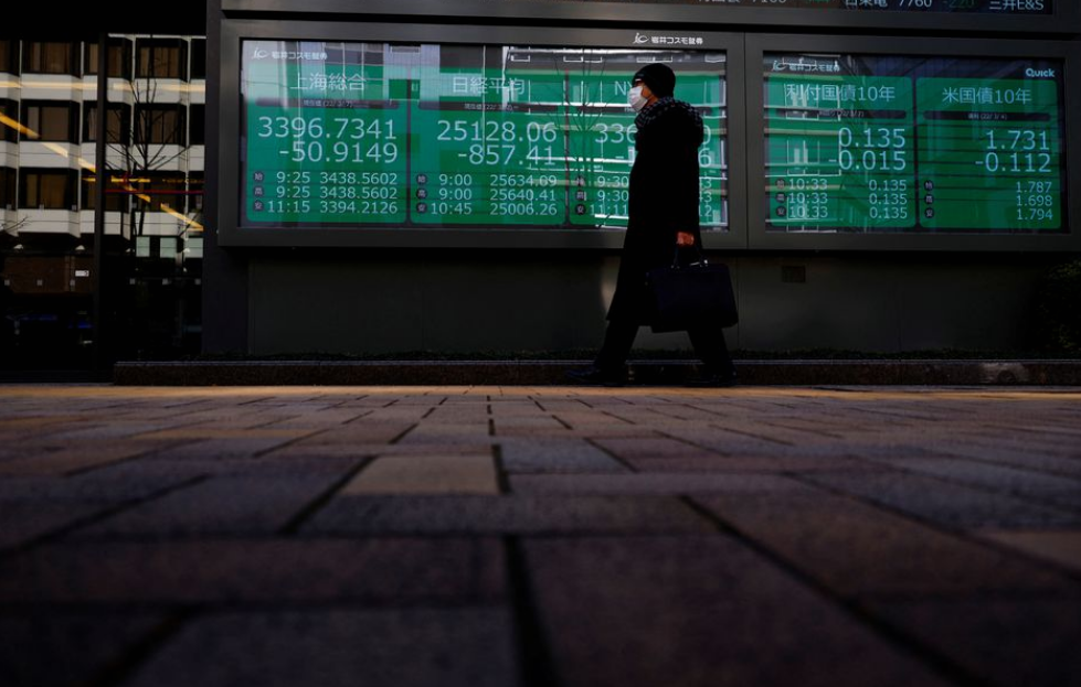 A man wearing a protective mask, amid the coronavirus disease (COVID-19) outbreak, walks past an electronic board displaying Shanghai Composite index,...