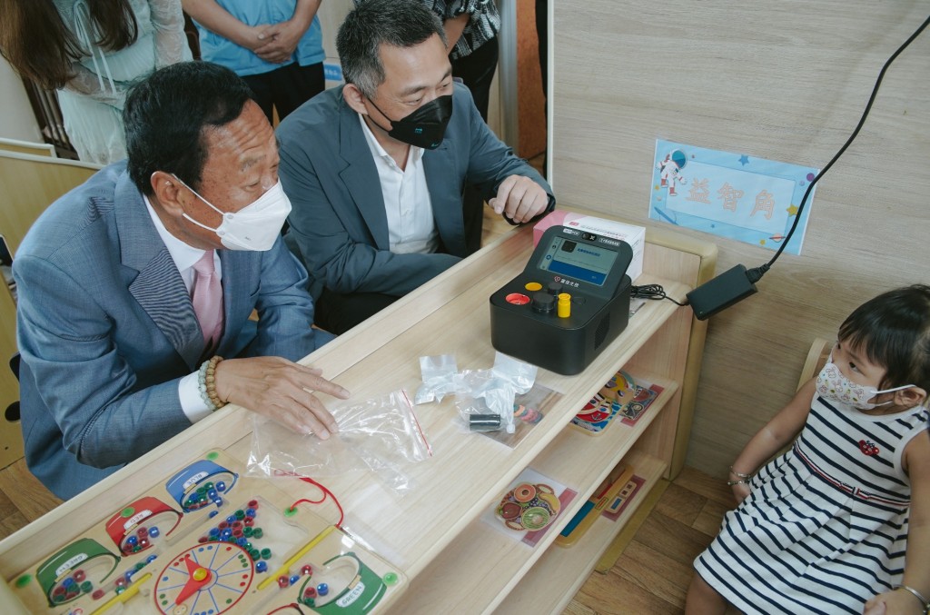 Terry Gou (left) sits near PCR device as he interacts with a small child. (Facebook, Terry Gou photo)
