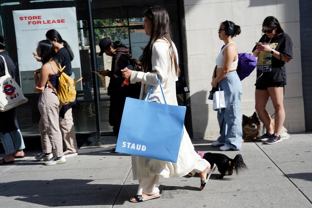 A woman carrying a shopping bag from Staud walks past people queuing for a pop-up&nbs...
