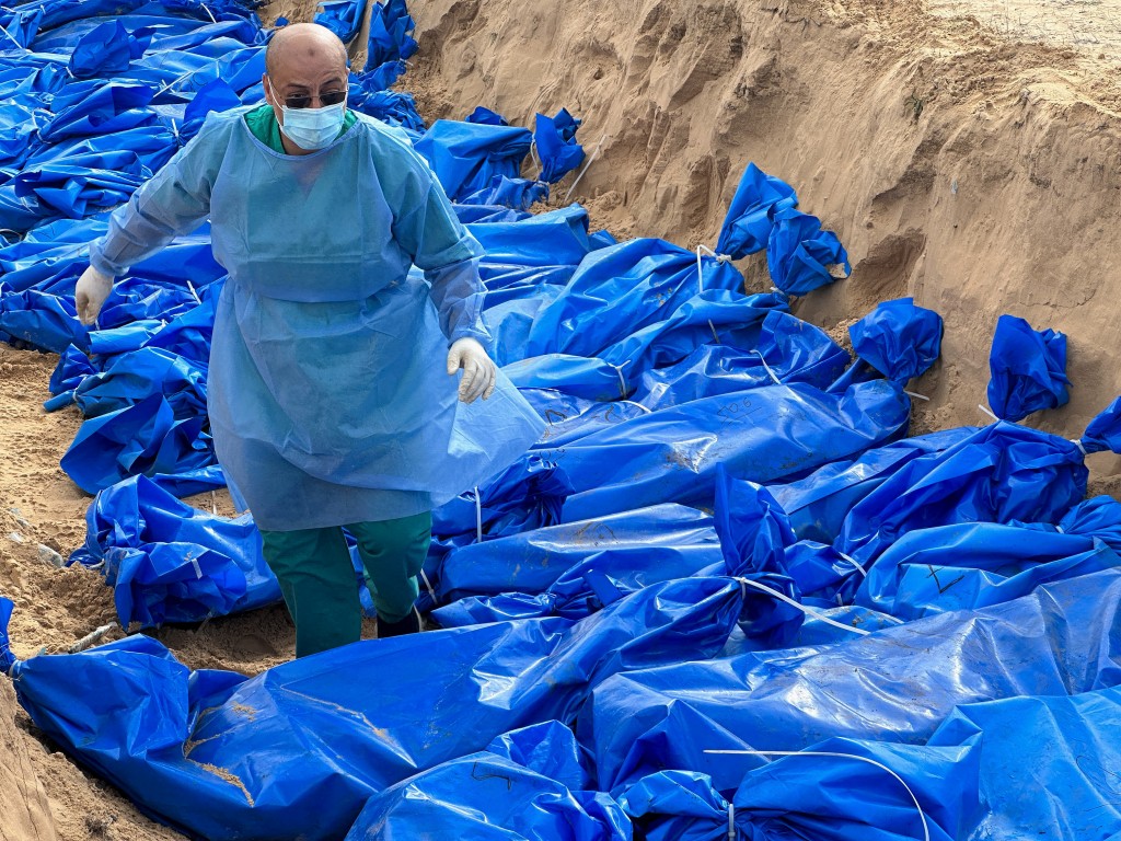 A man walks among the bodies of Palestinians killed in Israeli strikes and fire, as they are buried in a mass grave, after they were transported from ...