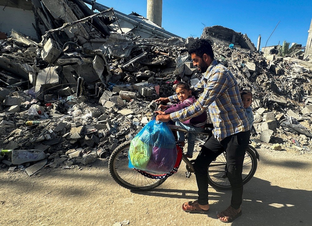 在以巴衝突停戰期間，一名巴勒斯坦男子推著腳踏車返回家園，路過一棟被以色列摧毀的屋子（圖／路透社MOHAMMED SALEM）
