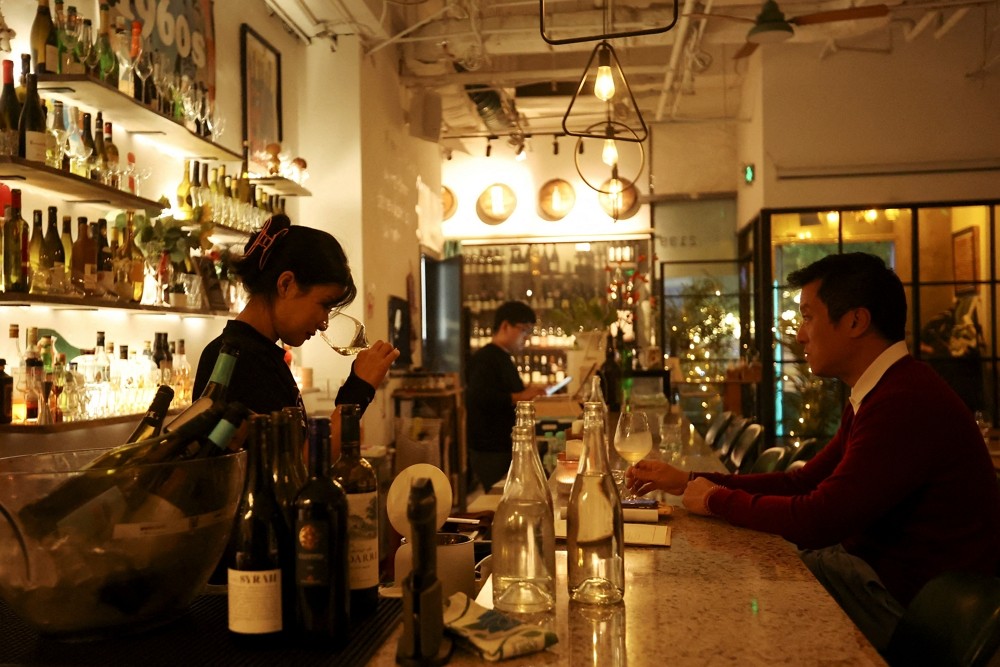 A staff member sniffs wine in a glass while a customer watches at theTrio Wine B...