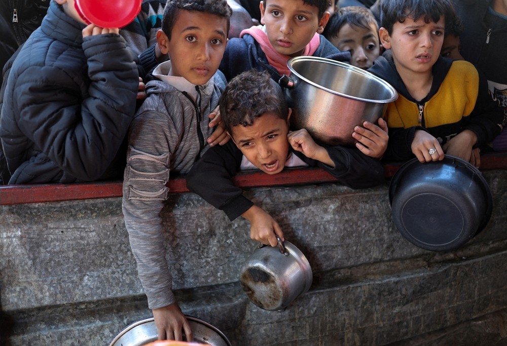 Palestinian children wait to receive food cooked by a charity kitchen amid shortages of food supplies, as...