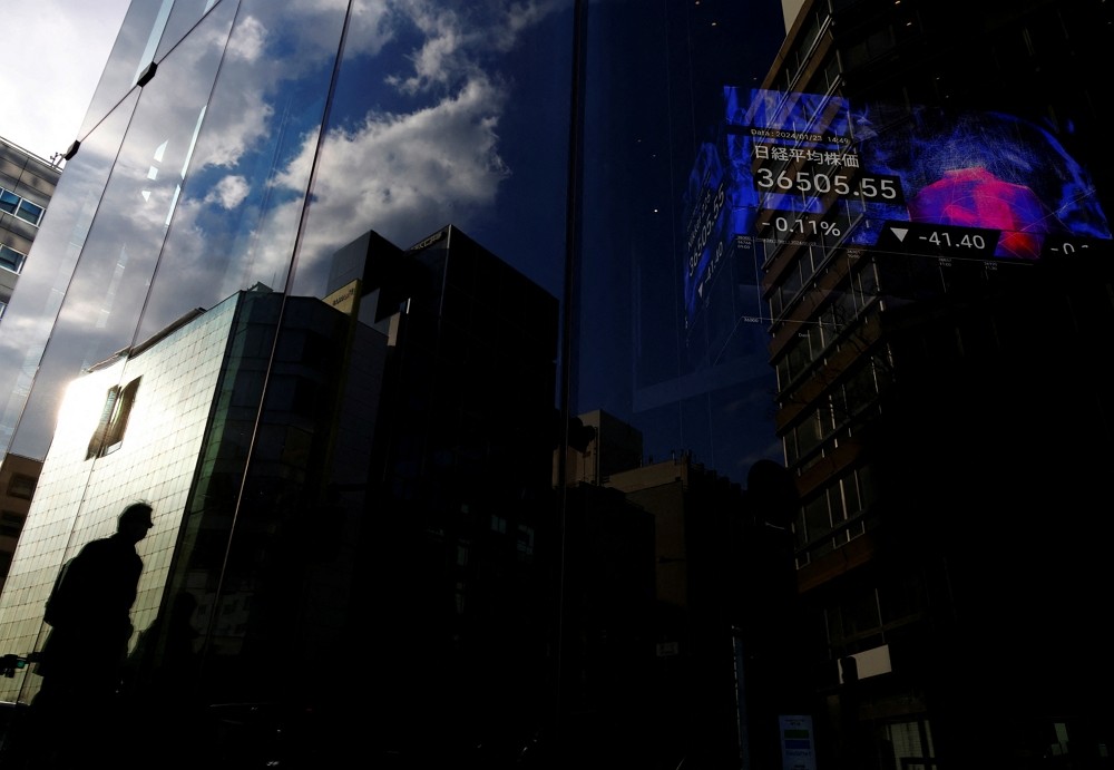 A pedestrian is reflected on a glass of a business building while an electric board showing Nikkei index is seen in the building at a busine...